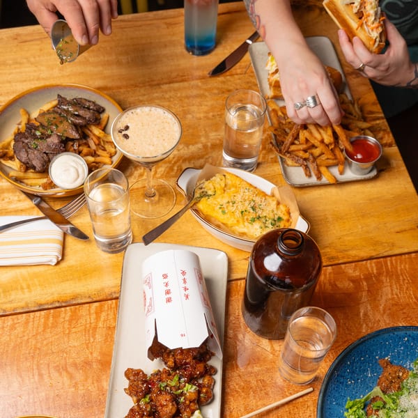 Overhead view of a wooden table laden with various dishes, drinks, and hands reaching for food.