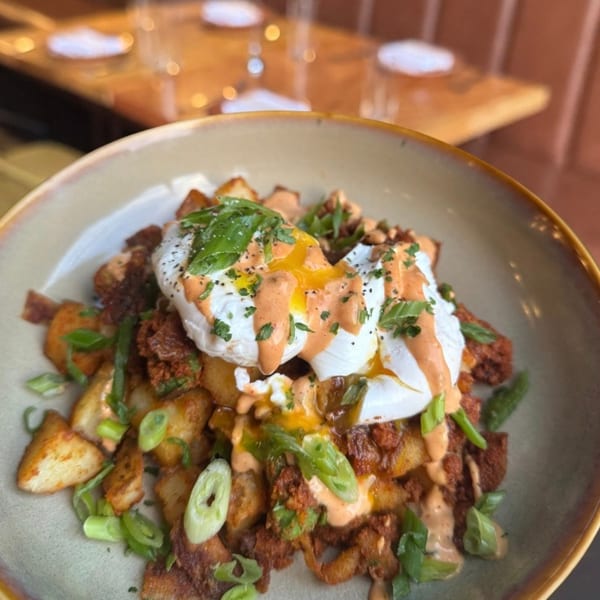 Close-up of a breakfast bowl with potatoes, chorizo, poached eggs, and green onions.